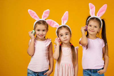 Portrait of happy friends holding heart shape against yellow background