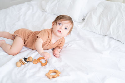 Cute baby girl lying by toys on bed at home