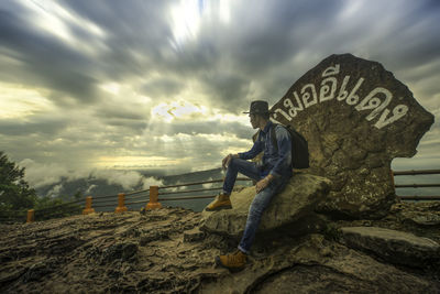 Side view of man sitting on land against sky