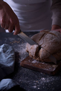 Hands slicing fresh bread, on dark background.