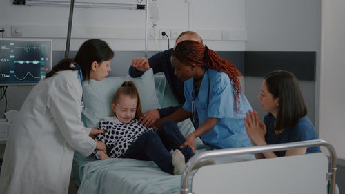 Doctor and parent assisting girl on bed at hospital