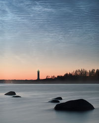 Silhouette lighthouse by sea against sky during sunset