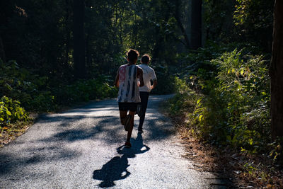 Rear view of men running in road amidst trees