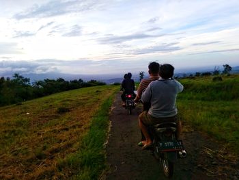 Rear view of people riding bicycle on field against sky