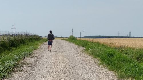 Rear view of man walking on road against clear sky