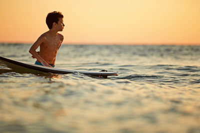 Young woman swimming in sea against sky during sunset