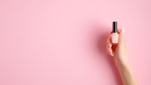 Close-up of hand holding pink petals against wall