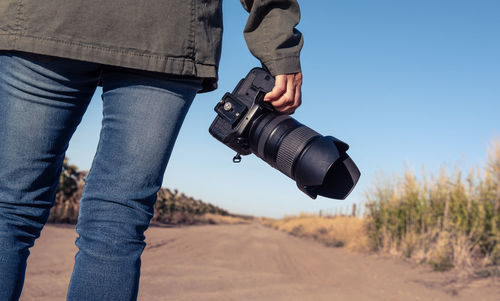 Midsection of woman holding camera while standing outdoors