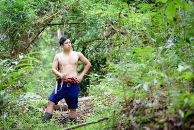 Full length of shirtless man standing in forest