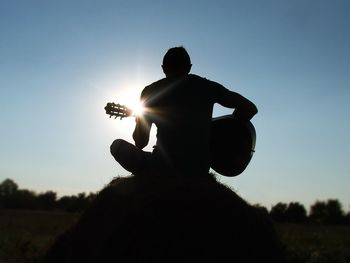 Silhouette man playing guitar against clear sky