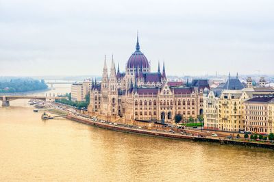 Buildings by river against sky in city