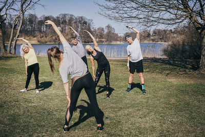 Rear view of instructor training senior people on field against lake at park