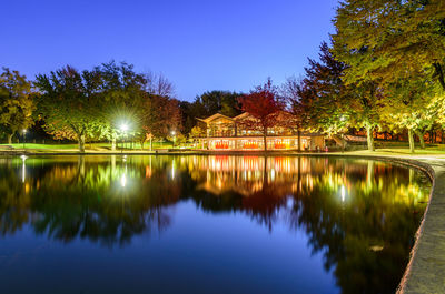 Scenic view of lake by trees and houses against clear blue sky