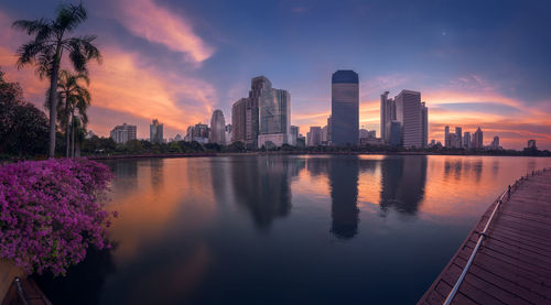 Scenic view of lake by buildings against sky during sunset