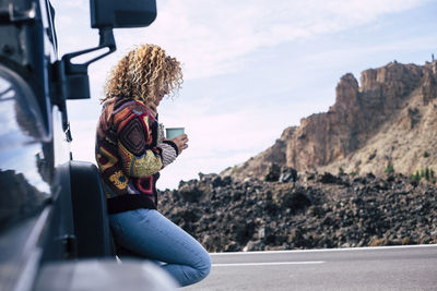 Woman having coffee while standing against car during winter