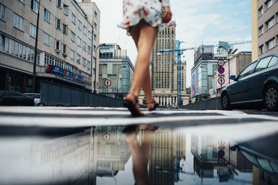 Reflection of woman on street against buildings in city