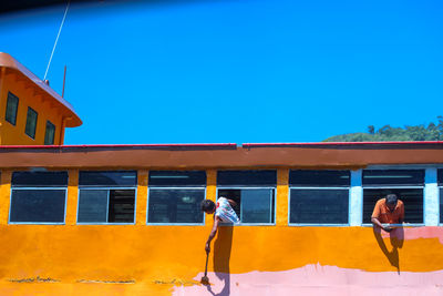 People standing by yellow window against blue sky