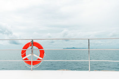 Orange color life buoy hanging on the rail of the luxury catamaran yacht with sea and sky.