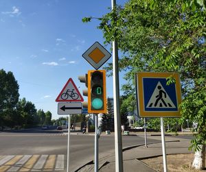 Road sign by trees in city against sky