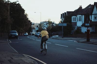 Rear view of person riding bicycle on road in city