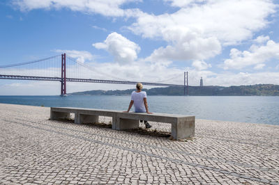 Woman sitting by 25 de abril bridge