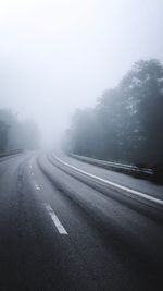 Road by trees against sky during winter