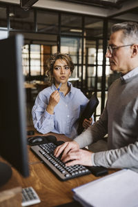 Female professional discussing with businessman using computer at desk