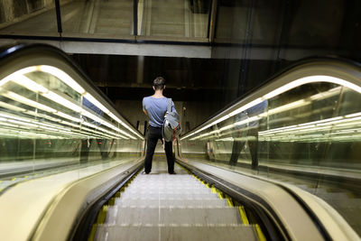 Young man with backpack standing on illuminated escalator at subway