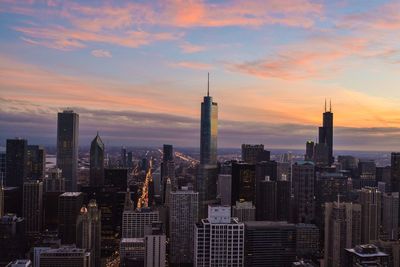 View of modern cityscape against cloudy sky during sunset