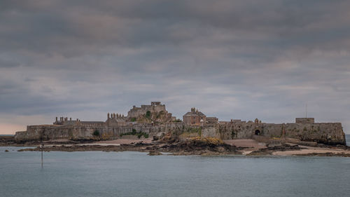 Buildings by sea against cloudy sky