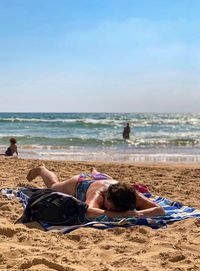 People relaxing on sand at beach against sky