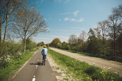 Rear view of woman riding bicycle against sky during sunny day