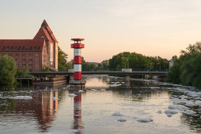 Building by lake against sky during sunset