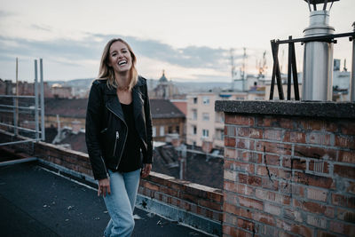 Full length of smiling young woman standing against sky in city