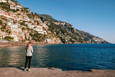 Rear view of woman standing by sea against clear blue sky