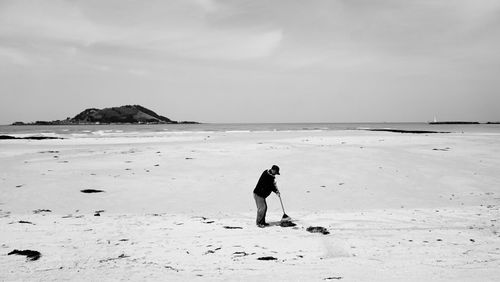 Man sweeping at beach against sky