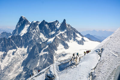 People hiking on snowcapped mountains against clear sky