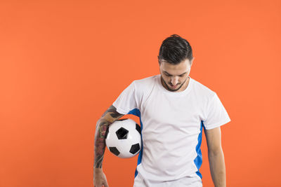 Side view of boy playing soccer ball against yellow background