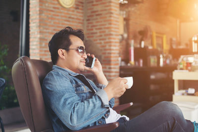 Young man holding coffee cup while using smart phone at cafe
