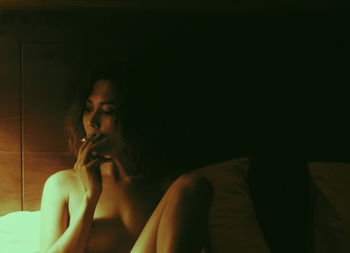 Young woman smoking while sitting in bedroom at home