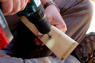 Cropped image of man using power tool on plank