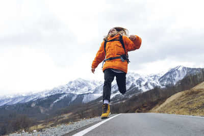 Carefree hiker jumping over mountain road in winter