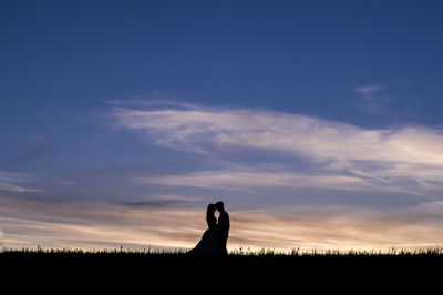 Silhouette couple on field against sky during sunset