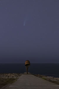Rear view of man standing by sea against sky at night