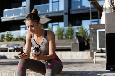 Young woman using smart phone while sitting outdoors