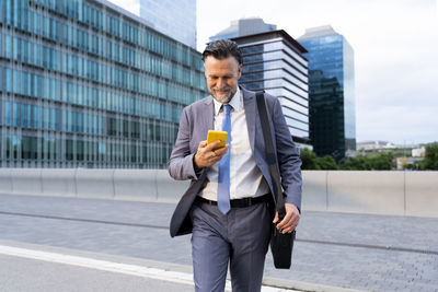 Smiling businessman using smart phone walking on street