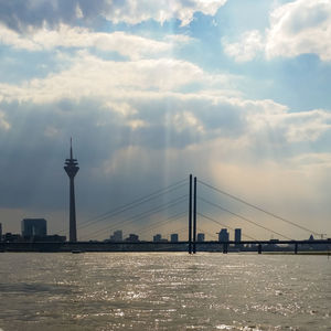 View of suspension bridge over river against cloudy sky