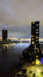 Illuminated city by river against sky at night