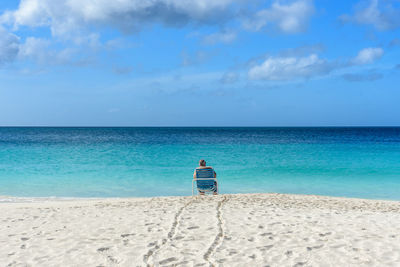 Rear view of man sitting on chair at beach