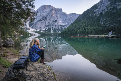 Woman sitting by lake against mountains
